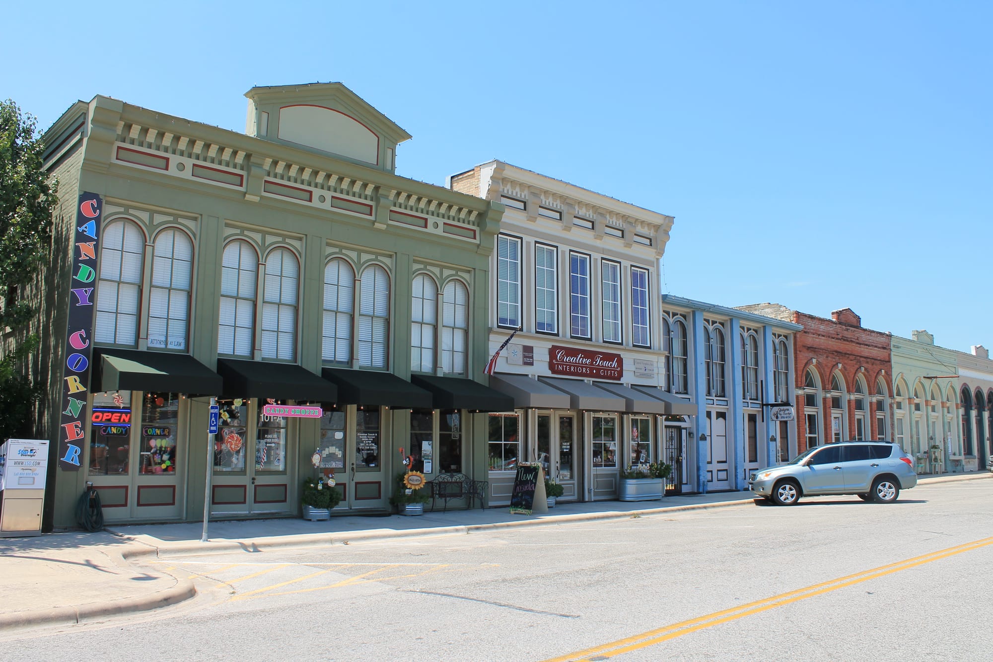 Restored two-story historic storefronts along a street in downtown Hutto, Texas, under a clear blue sky