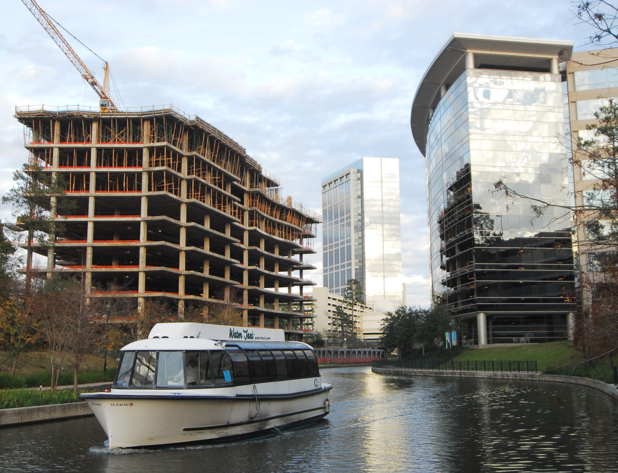 A water taxi on The Woodlands Waterway with glass office towers and a building under construction behind it